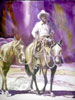This cow boy is riding against a purple sky and leading his pack horse while he is riding his own horse and all of them look to have traveled many a mile. 
