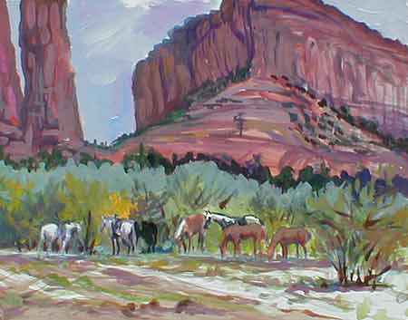 The navaho ponies stand by the Spider Rock Camp trees with the pink cliffs of the Arizona mountain in the distance at Canyon de Chelly.