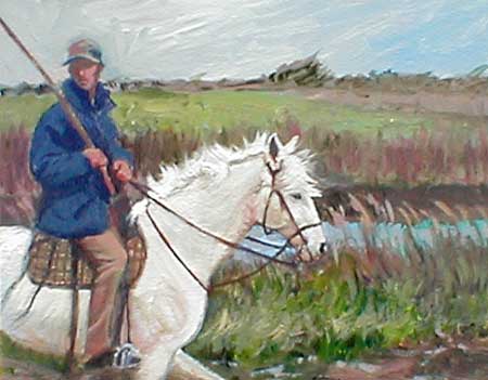This image is of a rider, riding a white horse, the rider is wearing a blue jacket and is riding by the marsh grass lands.
