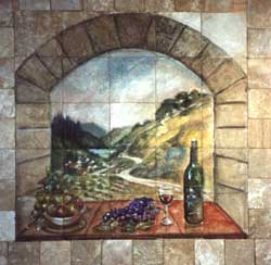 A tile painting of a stone window and a wine bottle and glass with grapes and fruit are sitting on the ledge. The window over looks a valley with a winding road and vineyards and hills.