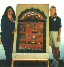 Karen and a friend are standing beside the tiles for the Ironwood Society.